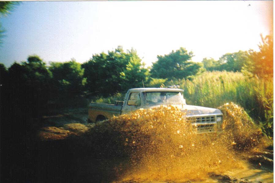 Light-colored Ford pickup slinging mud through an off-road mud hole