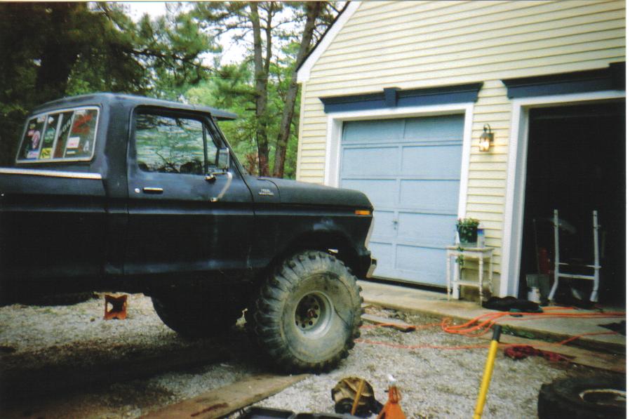 1979 Ford F-250 pickup truck, black, lifted with large off-road tires, parked in driveway next to garage