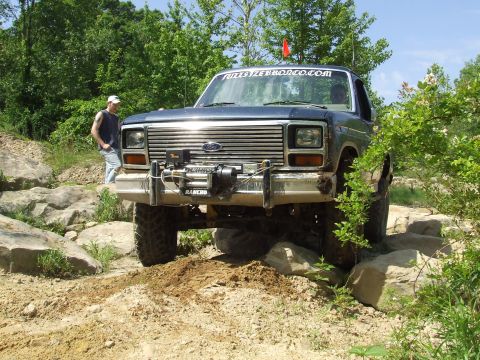1986 Ford Bronco - A dark blue Ford Bronco navigates a rocky trail with a winch mounted on the front bumper.