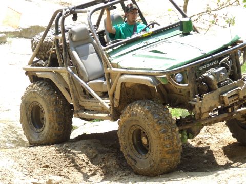 1986 Ford Bronco - A modified green off-road vehicle navigates a dirt track with a driver at the wheel.