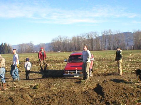 1978 Ford Bronco - A red SUV is stuck in a muddy field with several people observing.