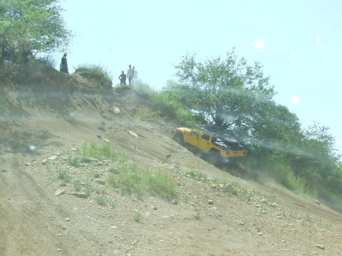 1986 Ford Bronco - A yellow Hummer H1 navigates a challenging off-road descent while onlookers observe from the ridge above.