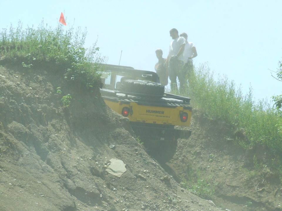 Yellow Hummer driving up a steep dirt incline with people watching