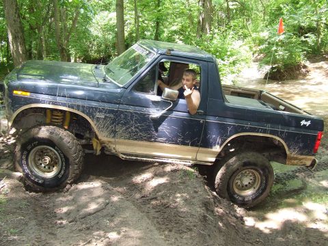 1986 Ford Bronco - A driver in a dark blue 1986 Ford Bronco navigates a muddy off-road trail.