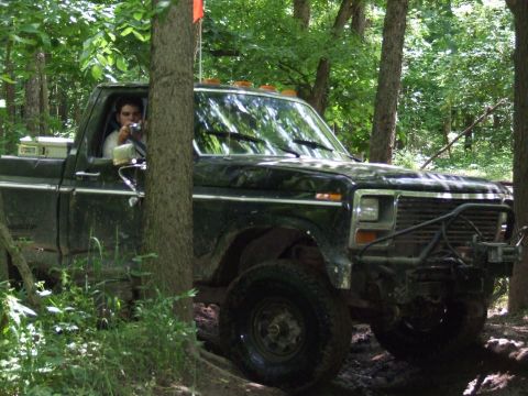 1986 Ford Bronco - A black pickup truck navigates a wooded trail with off-road tires and a brush guard.