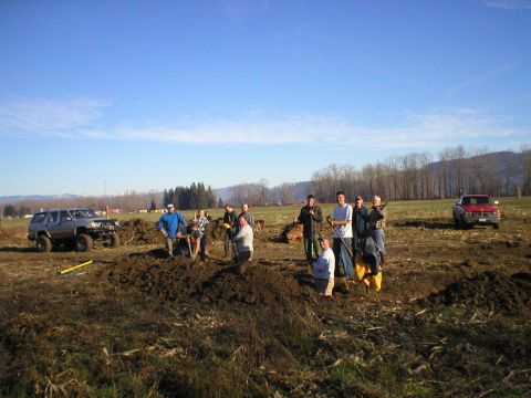 1978 Ford Bronco - People gathered in a muddy field with two vehicles present under a clear blue sky.