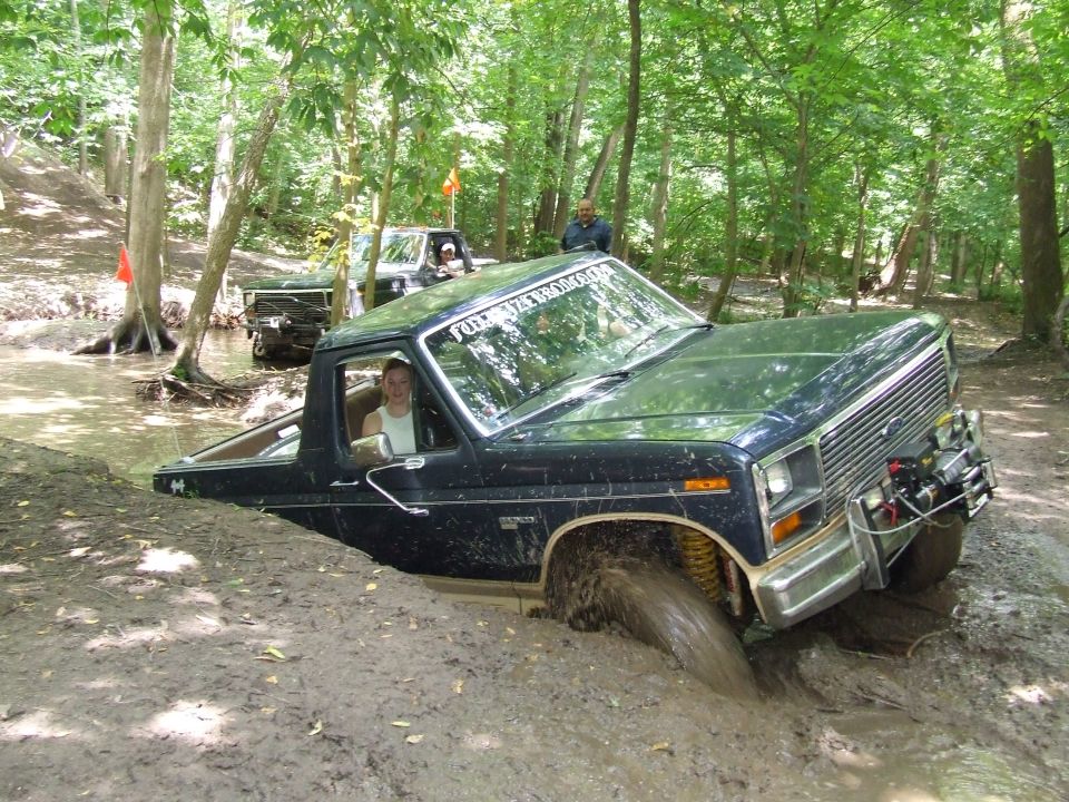 Dark blue 1986 Ford Bronco stuck in mud with winch on front bumper