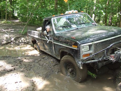 1986 Ford Bronco - Off-road pickup truck stuck in a muddy trail, surrounded by trees.