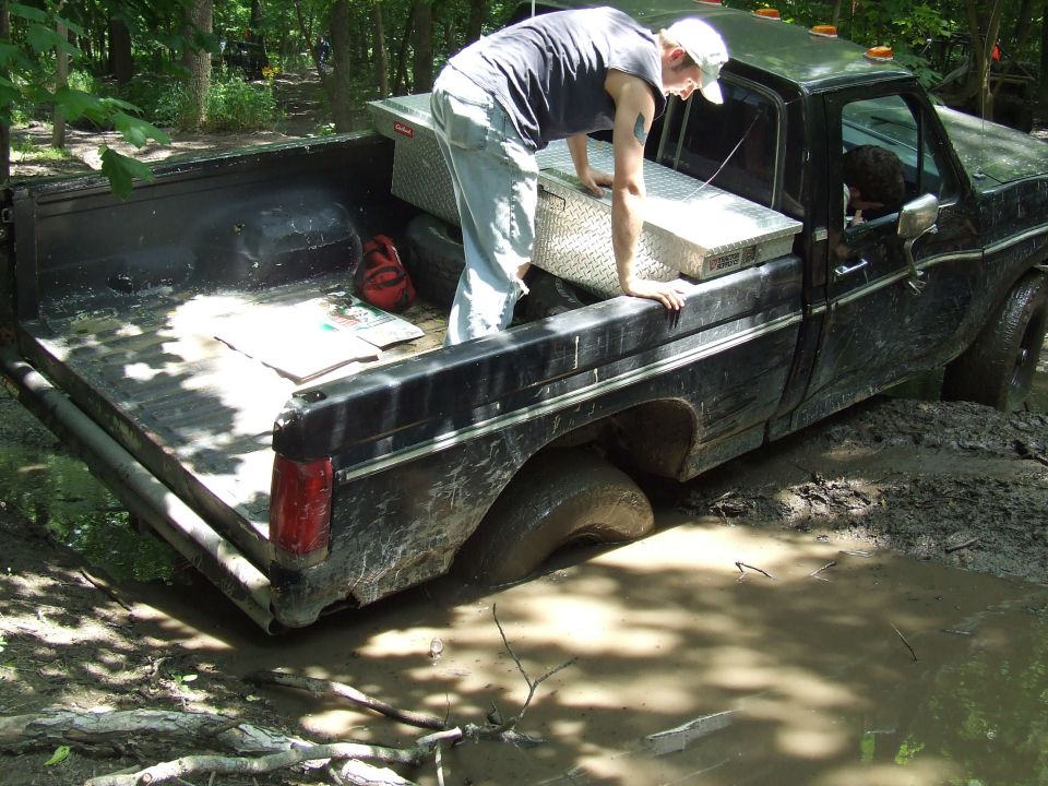 guy reaching into bed of black pickup truck stuck in mud, toolbox in bed