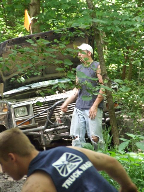 1986 Ford Bronco - A 1986 Ford Bronco sits in the woods with its hood open, attended by two people.