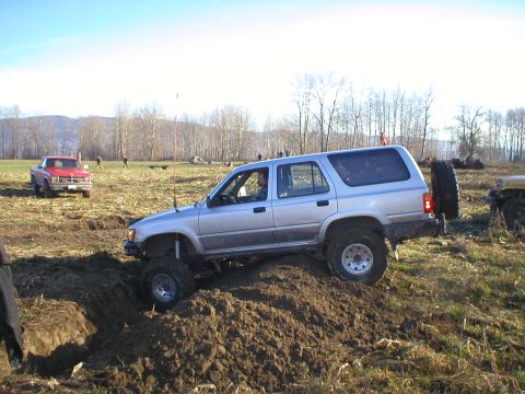1978 Ford Bronco - A silver Toyota 4Runner navigates a muddy obstacle course, with another vehicle visible in the distance.