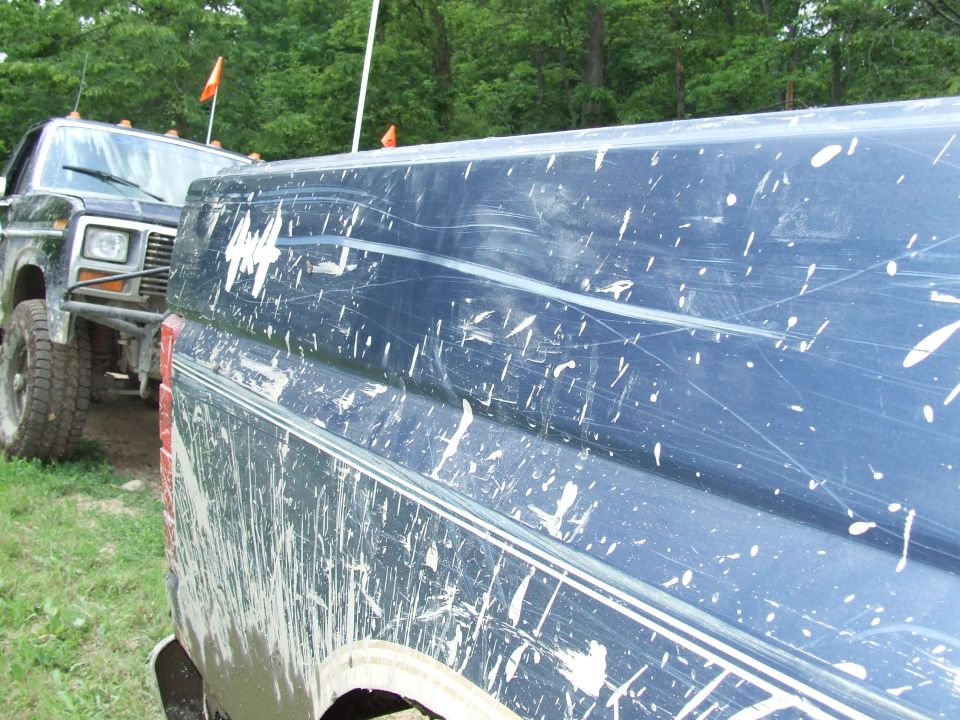 Mud-splattered dark blue Ford truck side with chrome trim and a dented fender