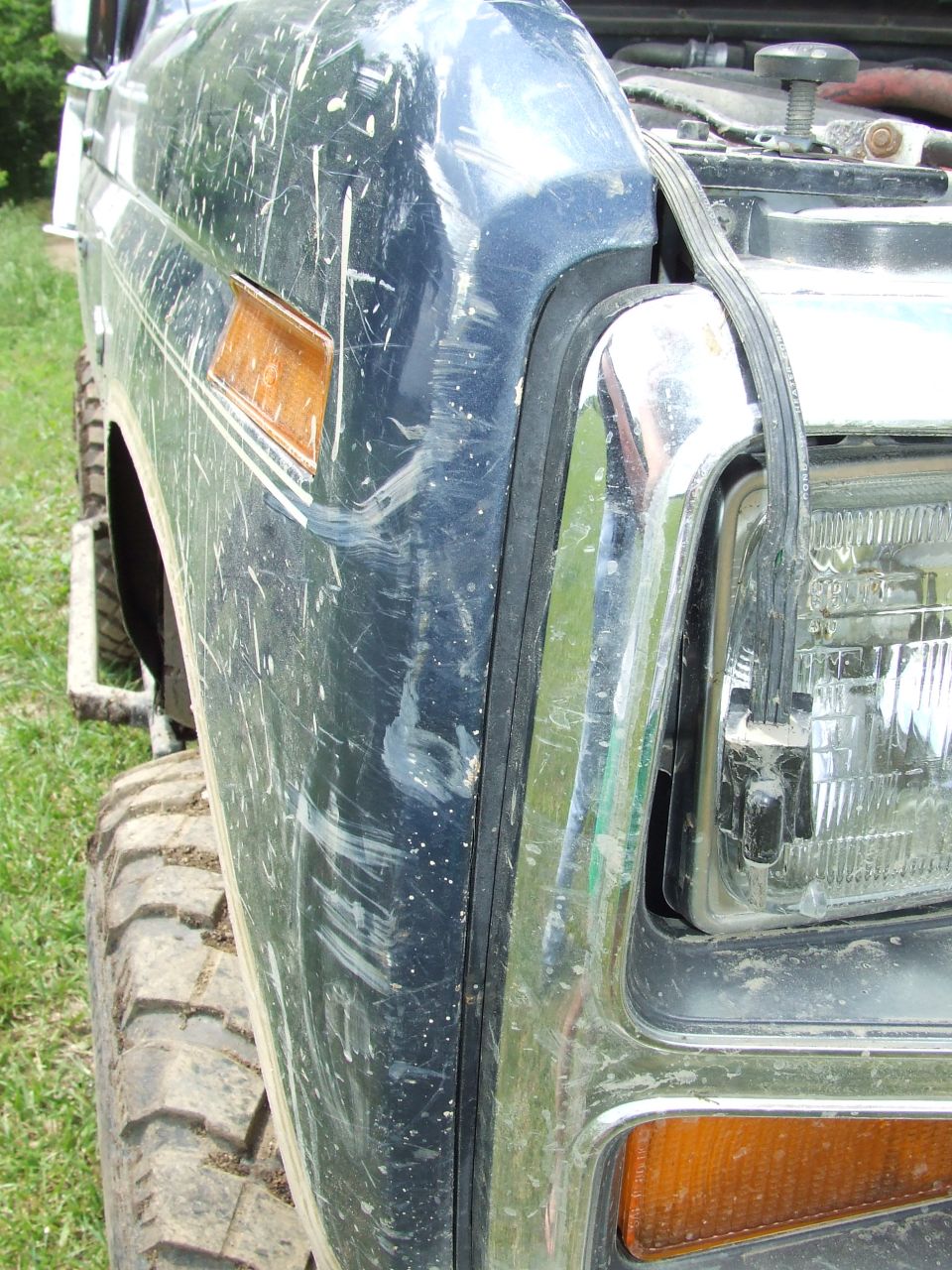 1986 Ford Bronco front fender, headlight, and grille detail. Scratched dark blue paint