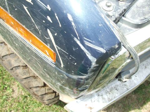 1986 Ford Bronco - The front corner of a blue vehicle shows significant damage, including scratches and dents.