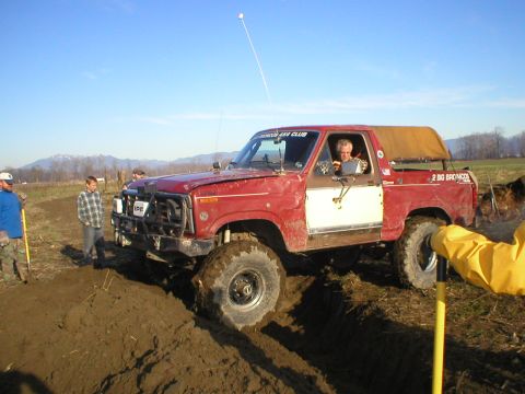 1978 Ford Bronco - A red 1978 Ford Bronco is stuck in the mud, with a driver visible behind the wheel and other people nearby.