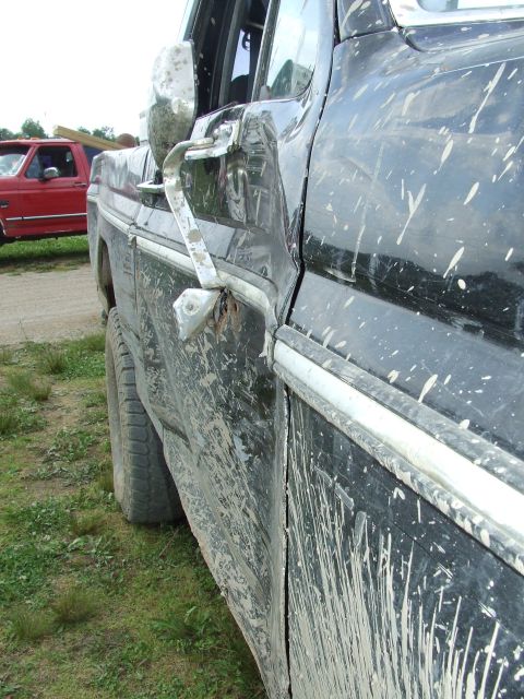 1986 Ford Bronco - Mud-covered 1986 Ford Bronco side profile with a damaged mirror and another red truck in the background.