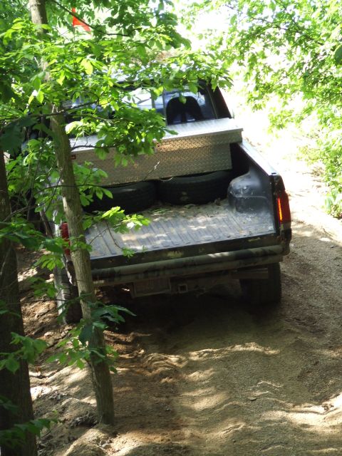1986 Ford Bronco - A pickup truck navigates a wooded trail, its bed equipped with a diamond plate toolbox.