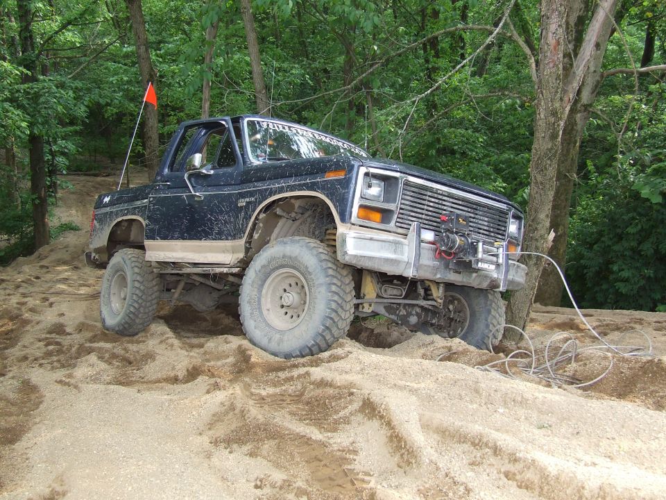 Dark blue Ford Bronco with large tires on a sandy hill, winch on front bumper