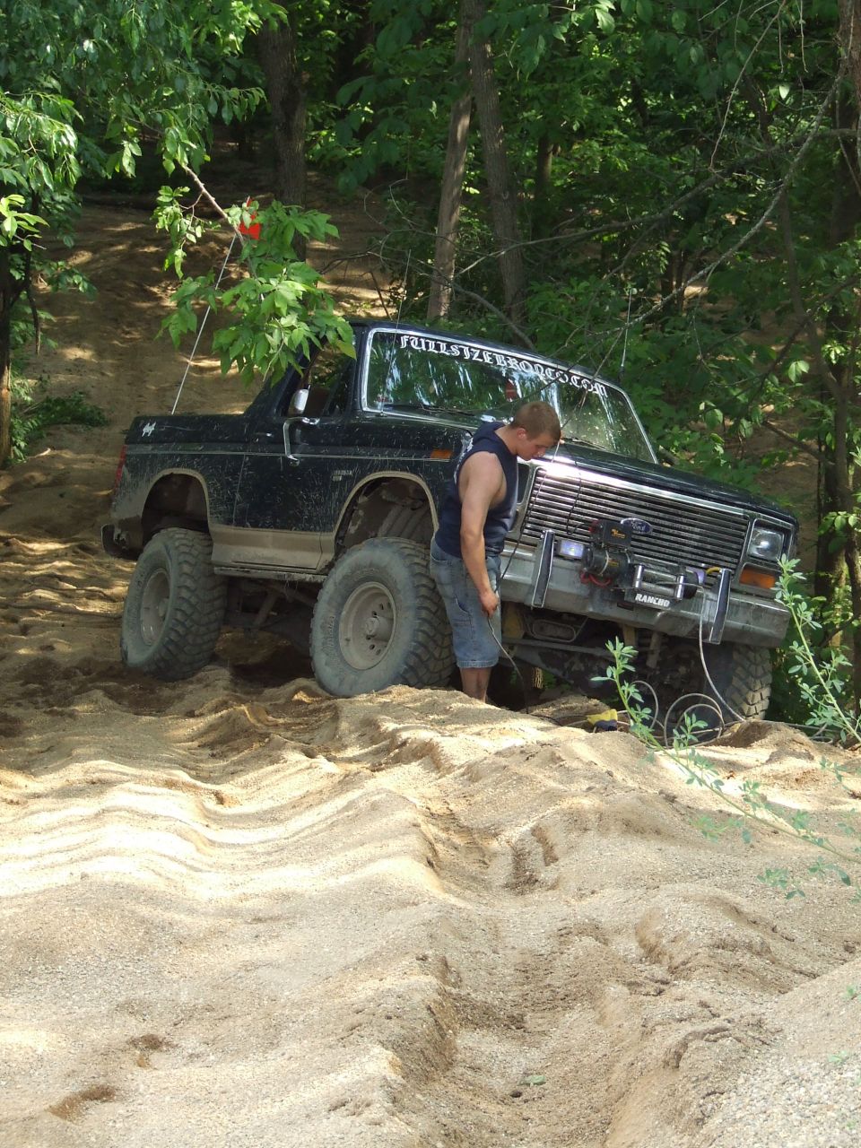 Black Ford Bronco with lifted suspension and large tires on a sandy incline