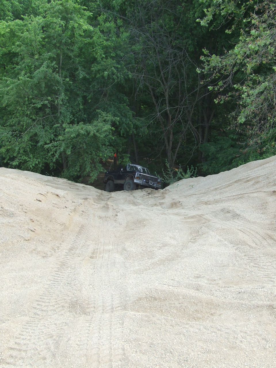 Black pickup truck climbing a sandy hill with trees in background