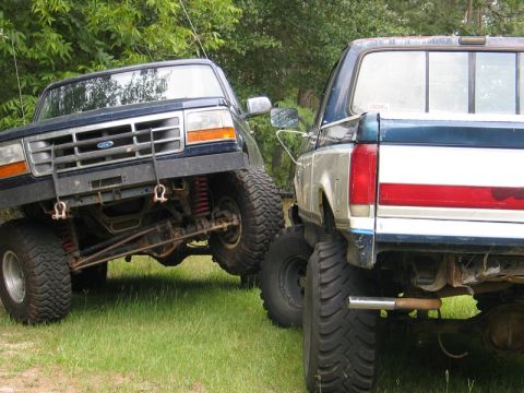 1989 Ford F-150 - Two lifted Ford F-Series trucks are parked outdoors, one in front of the other.