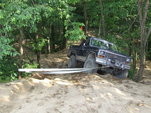 1986 Ford Bronco - This black SUV is navigating a sandy, wooded trail with a winch line attached.