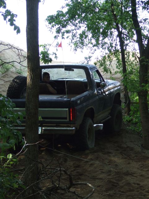 1986 Ford Bronco - A dark blue Ford Bronco navigates a dirt trail surrounded by trees.