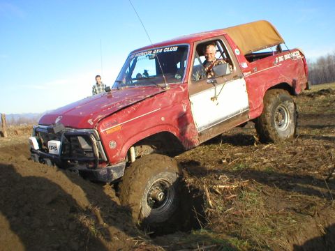 1978 Ford Bronco - This red SUV is stuck in the mud, with a driver and passenger visible. The windshield has club text.