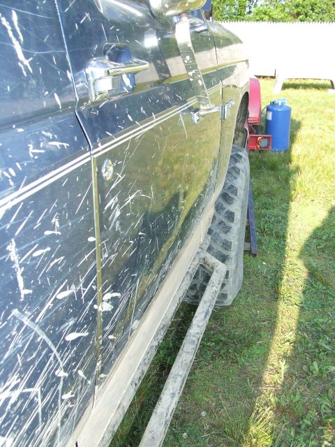 1986 Ford Bronco - Side view of a mud-splattered dark blue SUV with chrome trim and white racing stripes, parked on grass.