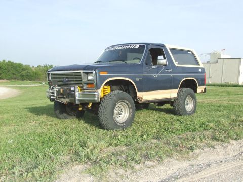 1986 Ford Bronco - Modified Ford Bronco with off-road tires and suspension sits in a grassy field.