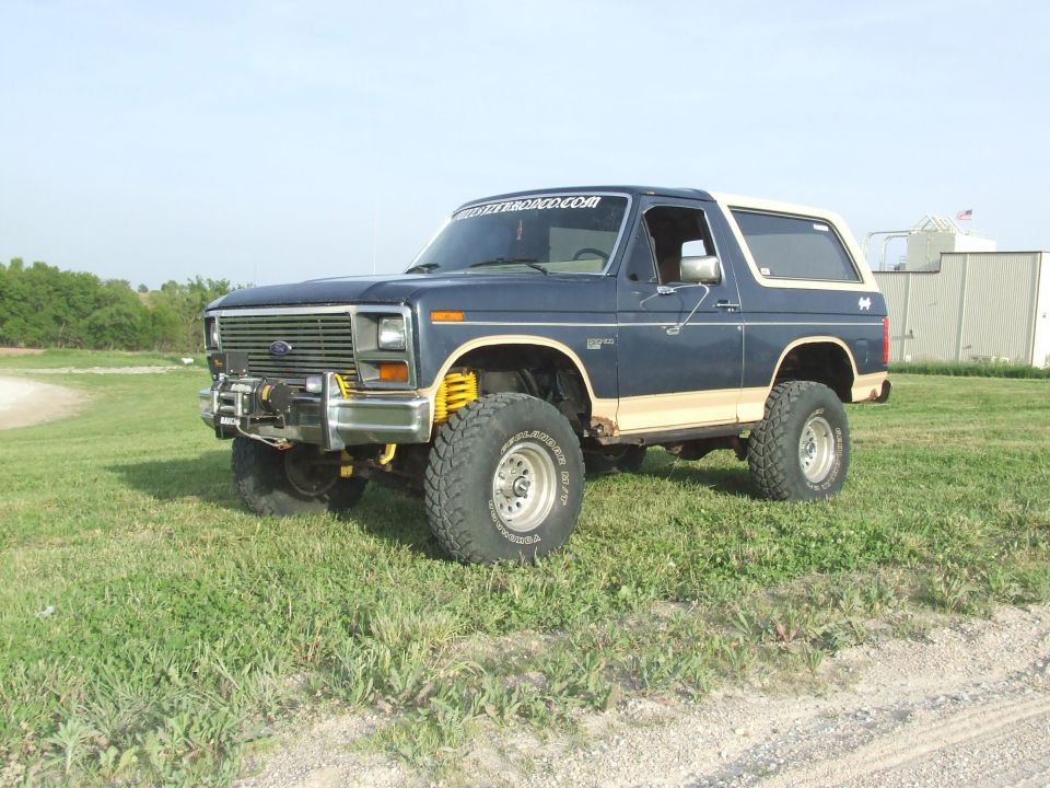 Blue 1980s Ford Bronco with tan trim, lifted suspension, and winch