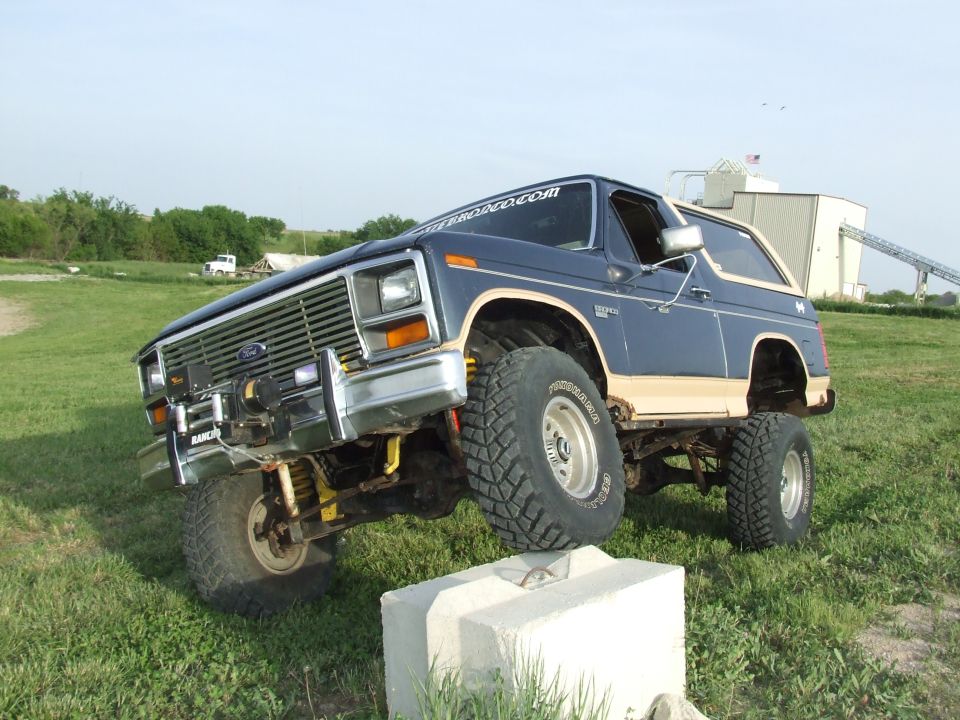 Lifted blue and tan Ford Bronco with front tire up on a concrete block showing suspension flex