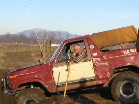 1978 Ford Bronco - A man drives a red and white 1978 Ford Bronco off-road, with mountains in the background.