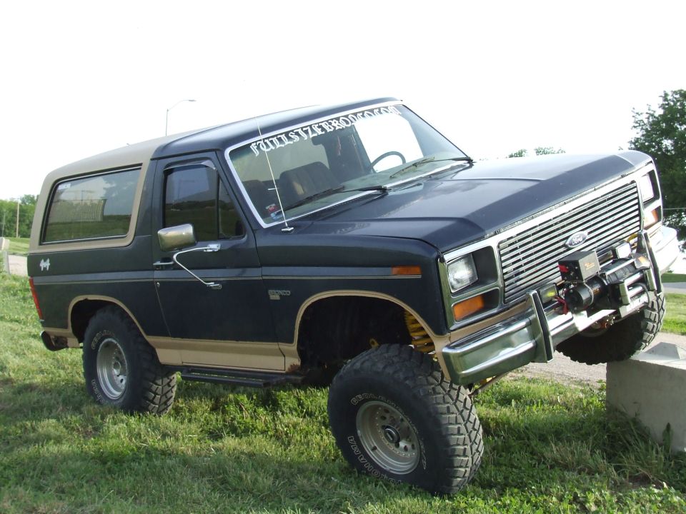 Lifted blue and tan Ford Bronco, 3/4 front view on grass with winch and mud-terrain tires