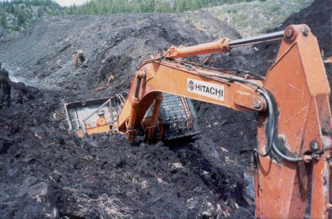 1990 Ford Bronco - An excavator operates in a challenging, muddy terrain with another machine visible in the distance.