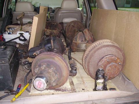 2000 Chevrolet Tahoe - Multiple vehicle axles and related parts are stored inside a vehicle's cargo area.