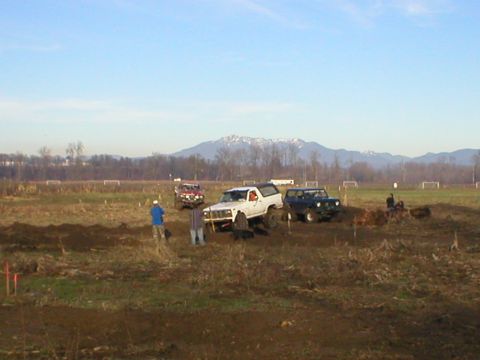1978 Ford Bronco - Multiple off-road vehicles navigate a dirt track under a clear sky with mountains visible in the distance.