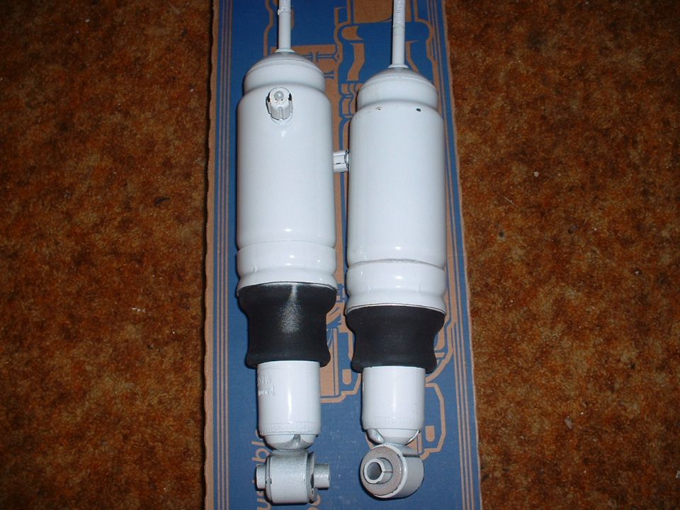 Two white shock absorbers with black rubber boots and silver mounting hardware, resting on a blue box