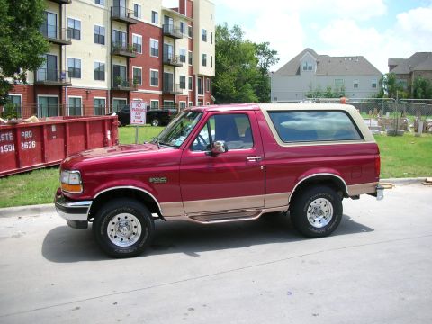 1995 Ford Bronco - Side profile of a red 1995 Ford Bronco with tan two-tone trim and a removable hardtop.