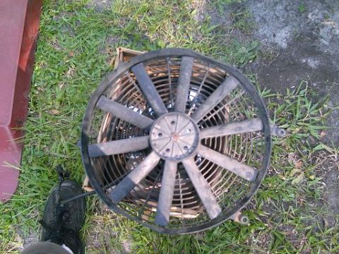 1986 Ford Bronco - A radiator fan is shown lying on the grass, with a portion of a red vehicle visible to the left.