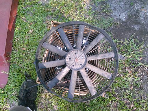 Radiator fan on grass next to a red vehicle panel