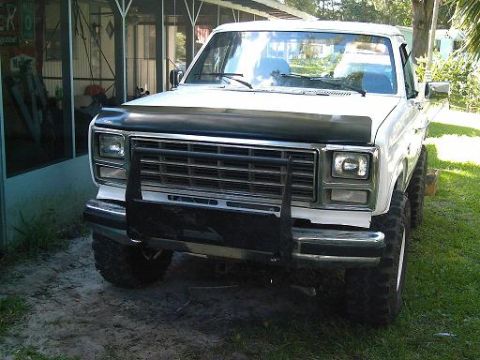 1986 Ford Bronco - This white SUV features a prominent black grille guard and oversized tires, seen from a 3/4 front angle.