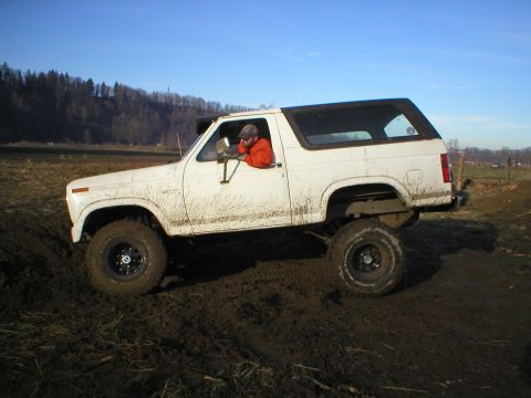 1978 Ford Bronco - A white Ford Bronco navigates a muddy terrain under a clear blue sky.