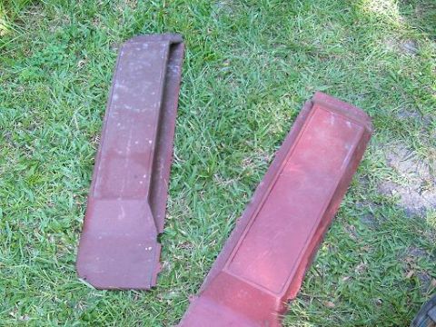 1986 Ford Bronco - Two red car trim pieces lie on the grass, suggesting they are parts from a vehicle.