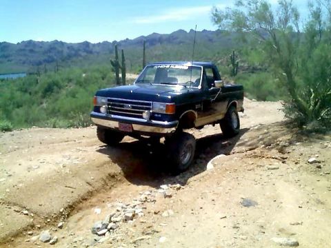 1991 Ford Bronco - A lifted 1987 Ford F-150 navigates a dusty desert trail with mountains and cacti in the background.