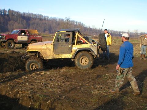 1978 Ford Bronco - A yellow Jeep Wrangler navigates a muddy off-road course, with a red Ford pickup truck visible behind it.