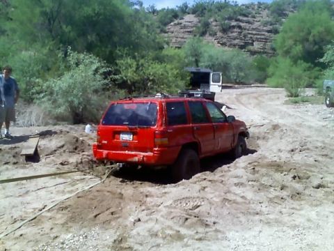 1991 Ford Bronco - A red SUV is stuck in the mud with a tow strap attached, while a man watches.