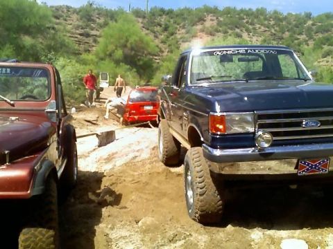 1991 Ford Bronco - A blue 1991 Ford Bronco navigates an off-road trail with other vehicles present.