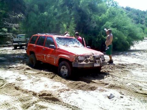 1991 Ford Bronco - A red Jeep Grand Cherokee is stuck in the sand with people around it.