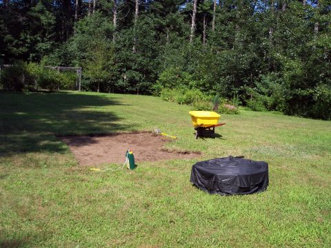 2001 Ford Crown Victoria - A backyard scene shows a yellow wheelbarrow and a tarp-covered object next to a prepared garden bed.
